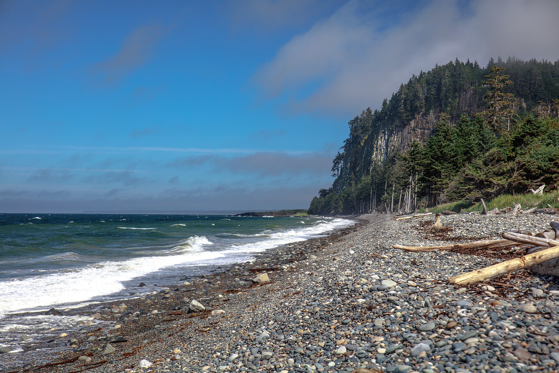 Pebbled Agate Beach curving toward the forested basalt cliff of Tow Hill