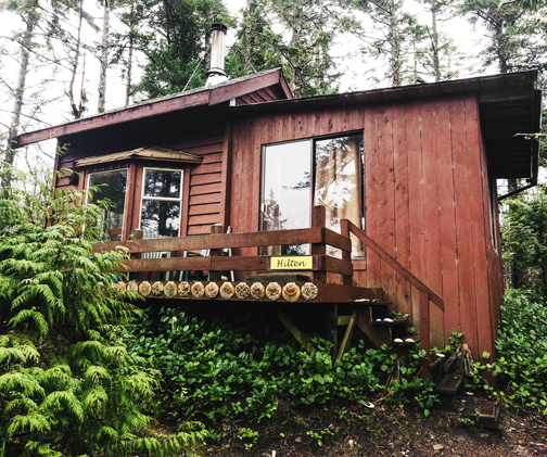The Hilten — a red post-and-beam cabin raised on a knoll among spruce and ferns